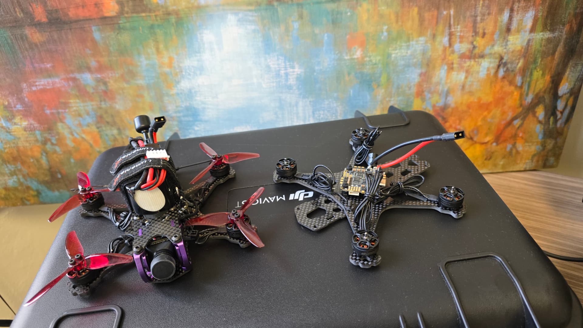 A completed racing drone sits beside a partially assembled drone frame with motors, wiring, and electronic components visible.